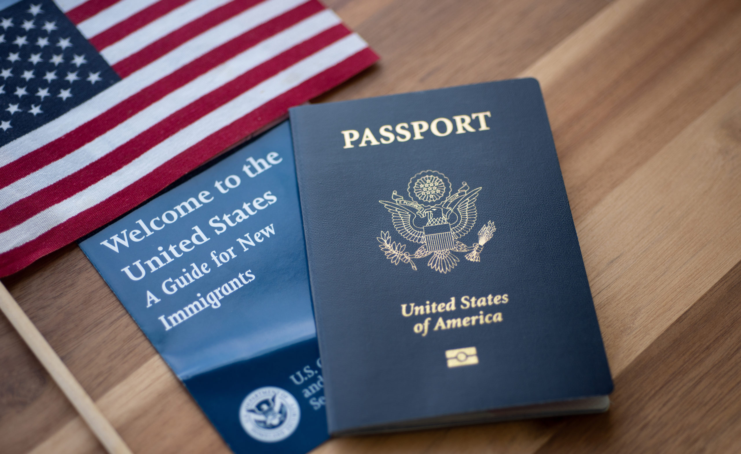 Passport of USA (United states of America) next to a Guide for new Immigrants Welcome to the United states and American Flag. Wooden Background.