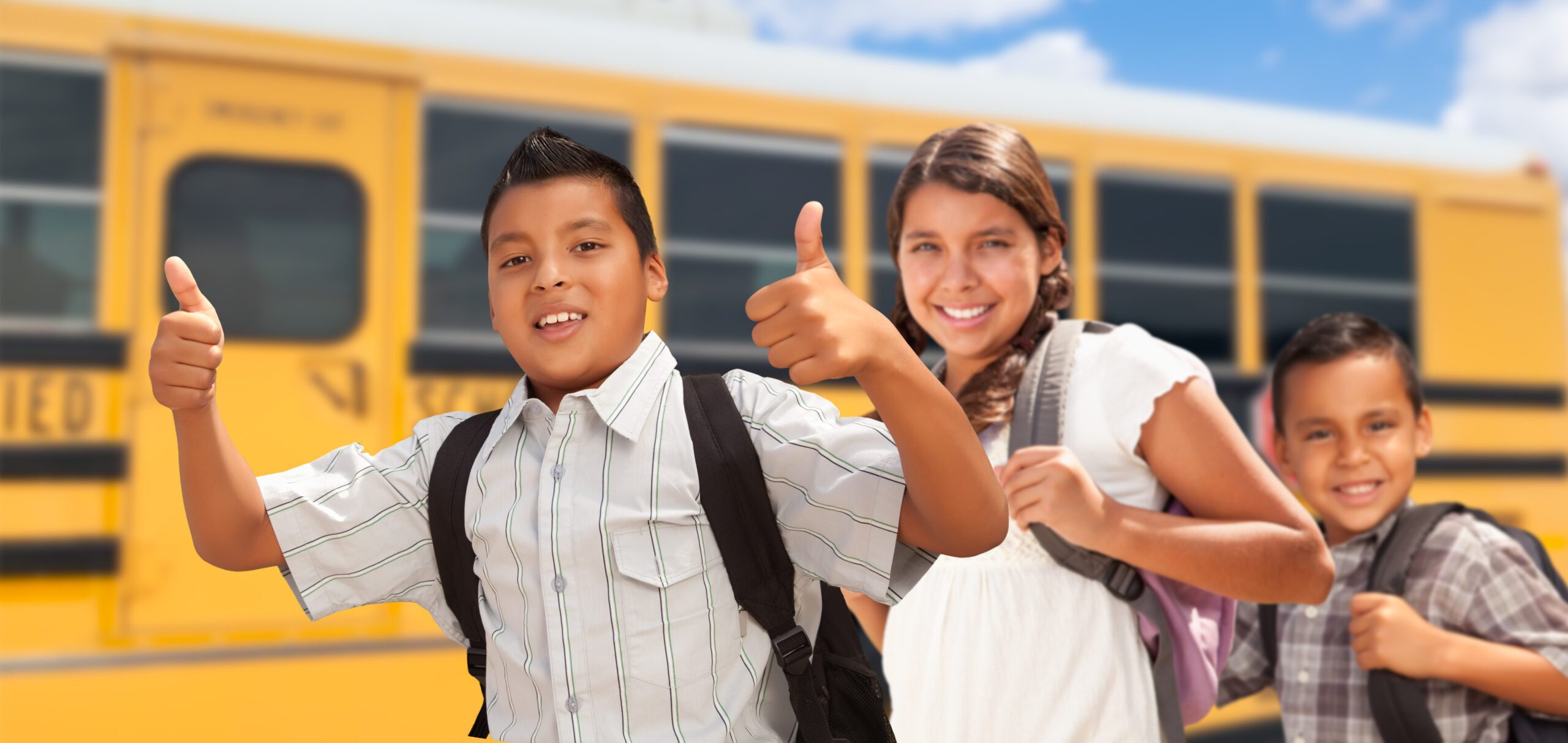 Young Hispanic Boys and Girl Walking Near School Bus.