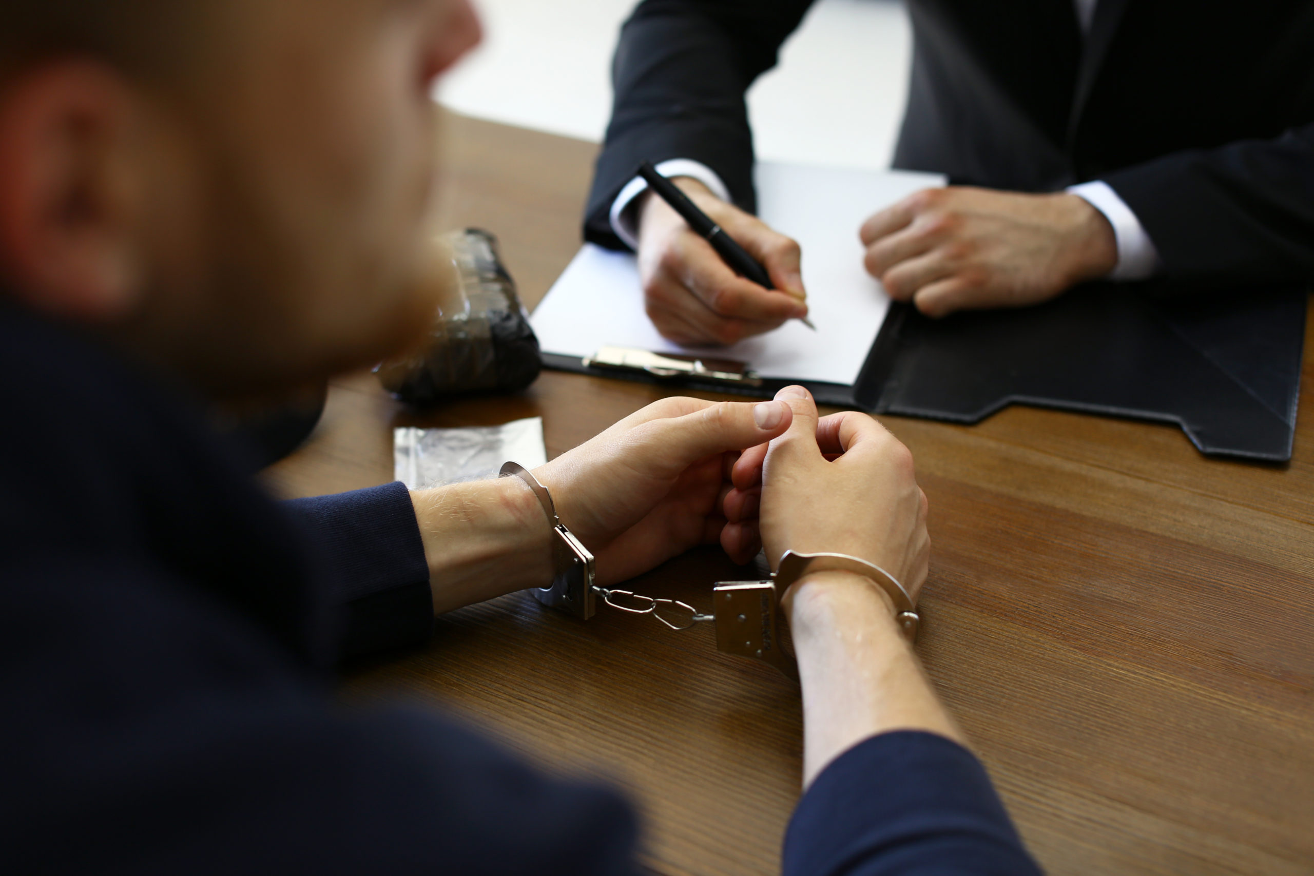 Police officer interrogating criminal in handcuffs at desk indoo